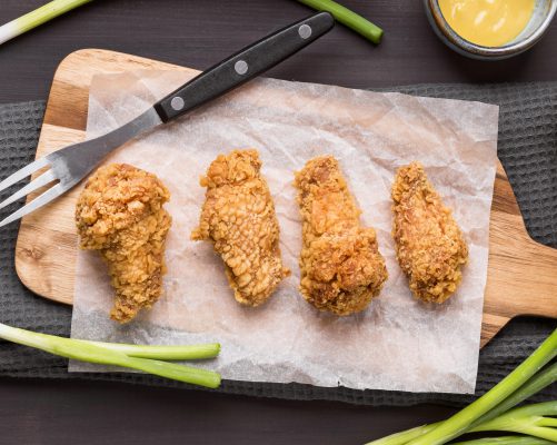 top view fried chicken wings cutting board with green onions fork